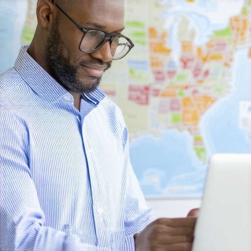 Business owner analyzing payroll data across multiple states using a laptop with a map in the background.